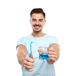 Young man holding toothbrush and glass with mouthwash on white background. Teeth care