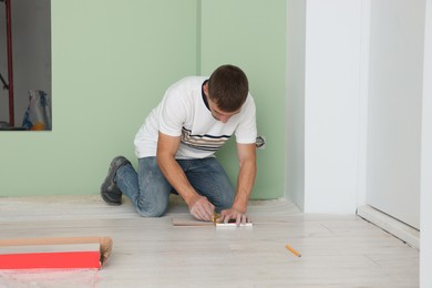 Photo of Man using pencil during installationnew laminate flooring in room