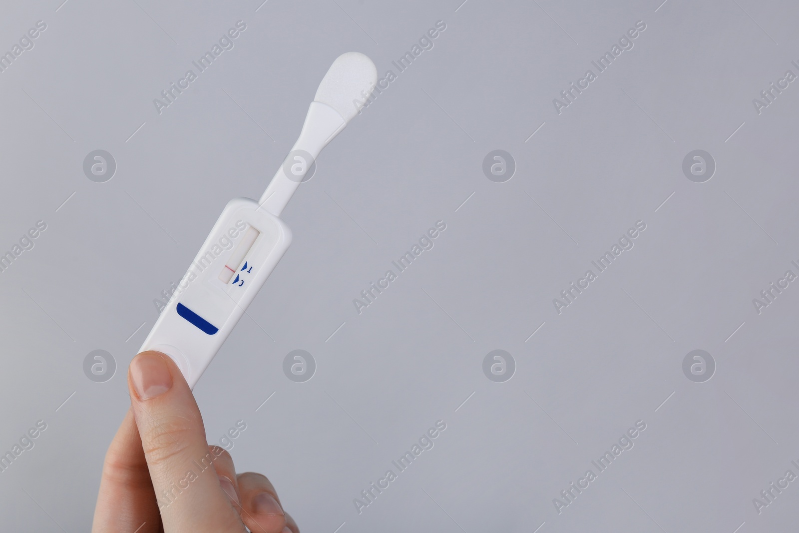 Photo of Woman holding disposable express test on light grey background, closeup. Space for text