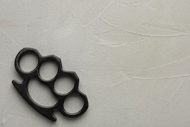 Photo of Black brass knuckles on light grey stone background, top view. Space for text