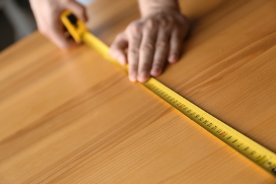 Photo of Man measuring wooden table, closeup. Construction tool