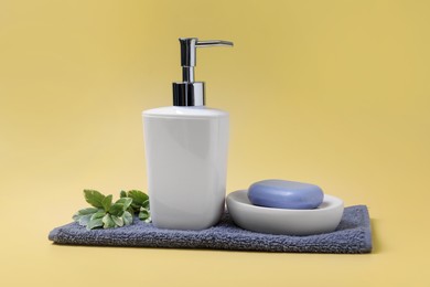 Photo of Soap bar, bottle dispenser and towel on yellow background