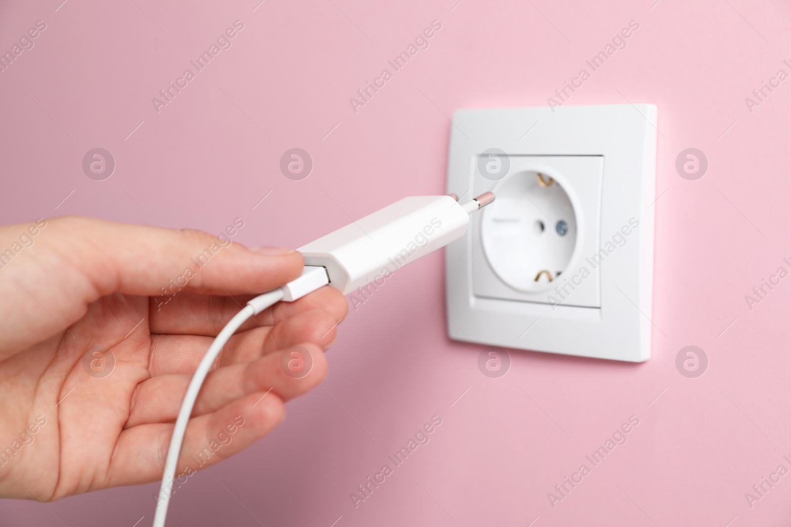 Photo of Woman plugging charger into power socket on pink wall, closeup. Electrical supply