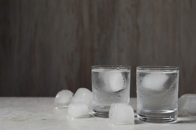 Photo of Shot glassesvodka with ice cubes on light grey table against wooden background. Space for text