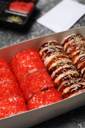 Different tasty sushi rolls in paper box on table, closeup