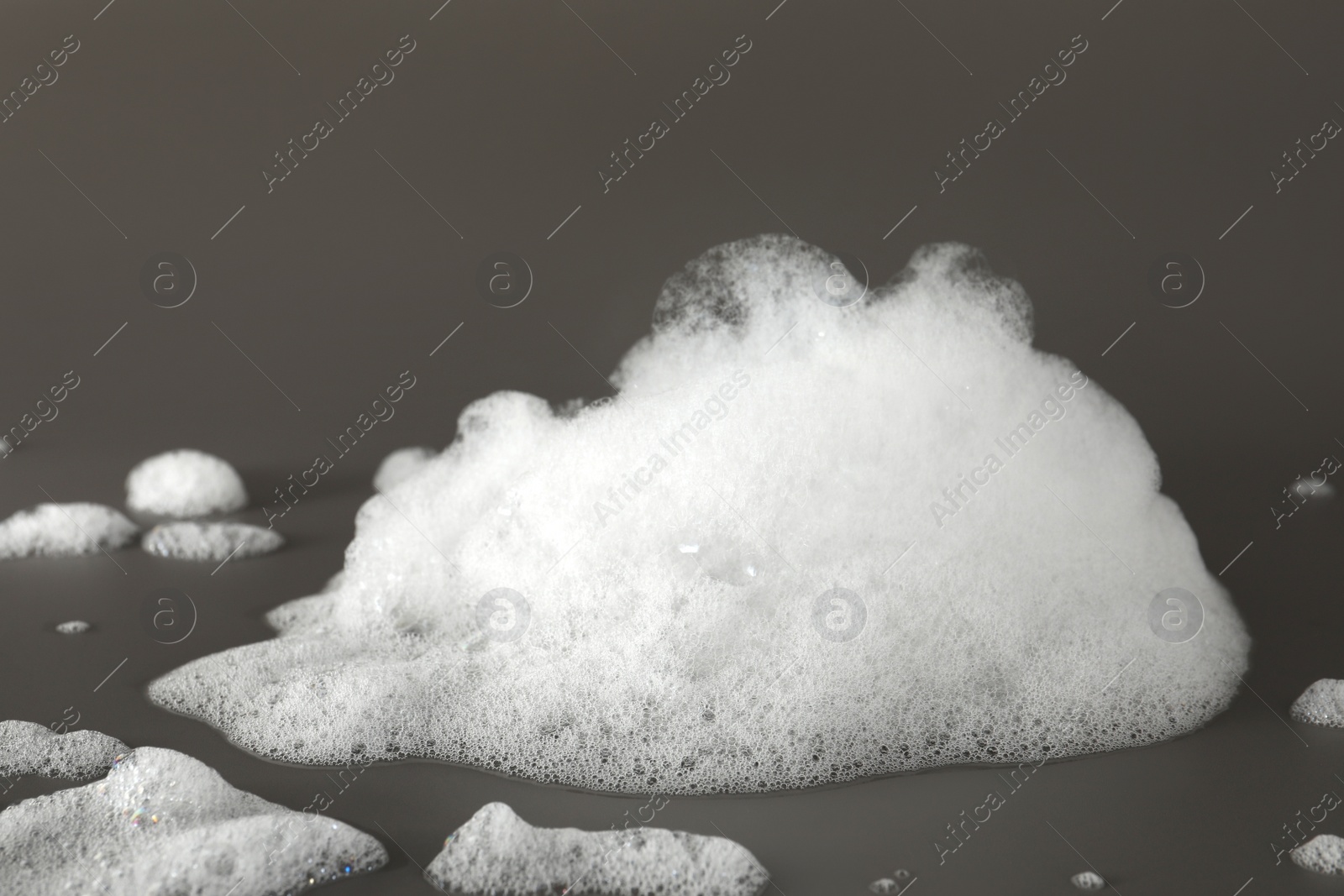 Photo of Fluffy bath foam on grey background, closeup