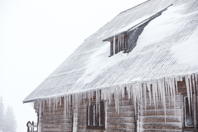 Photo of Wooden house with icicles on snowy day. Winter vacation