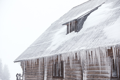 Wooden house with icicles on snowy day. Winter vacation