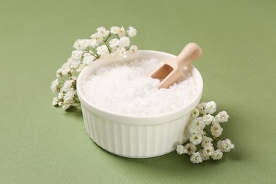 Bowl with sea salt and beautiful flowers on olive background