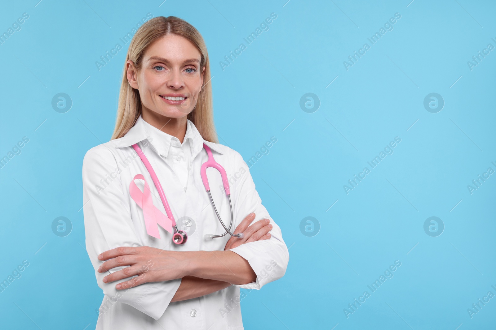 Photo of Doctor with pink ribbon and stethoscope on light blue background, space for text. Breast cancer awareness