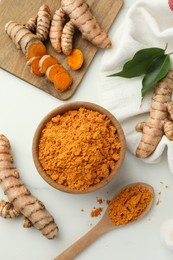 Photo of Aromatic turmeric powder, raw roots and green leaves on white table, flat lay
