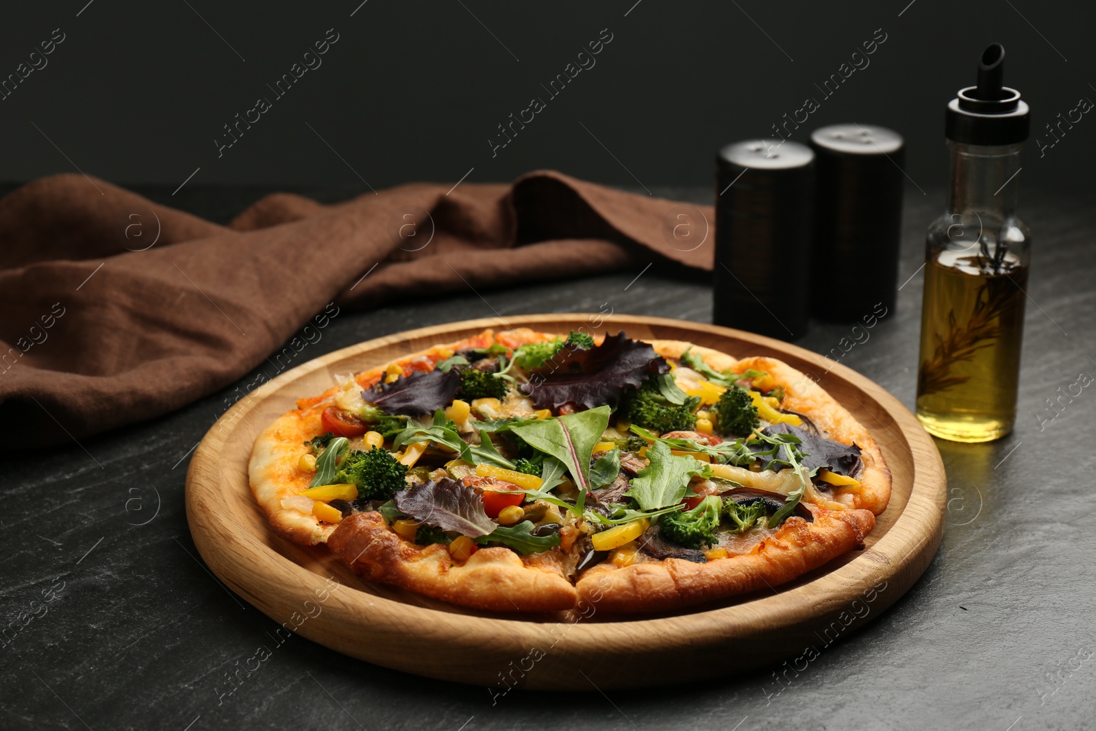 Photo of Delicious vegetarian pizza with vegetables and greens on black table