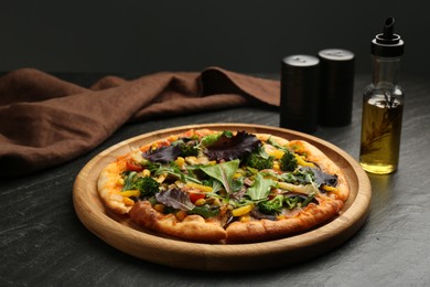 Photo of Delicious vegetarian pizza with vegetables and greens on black table