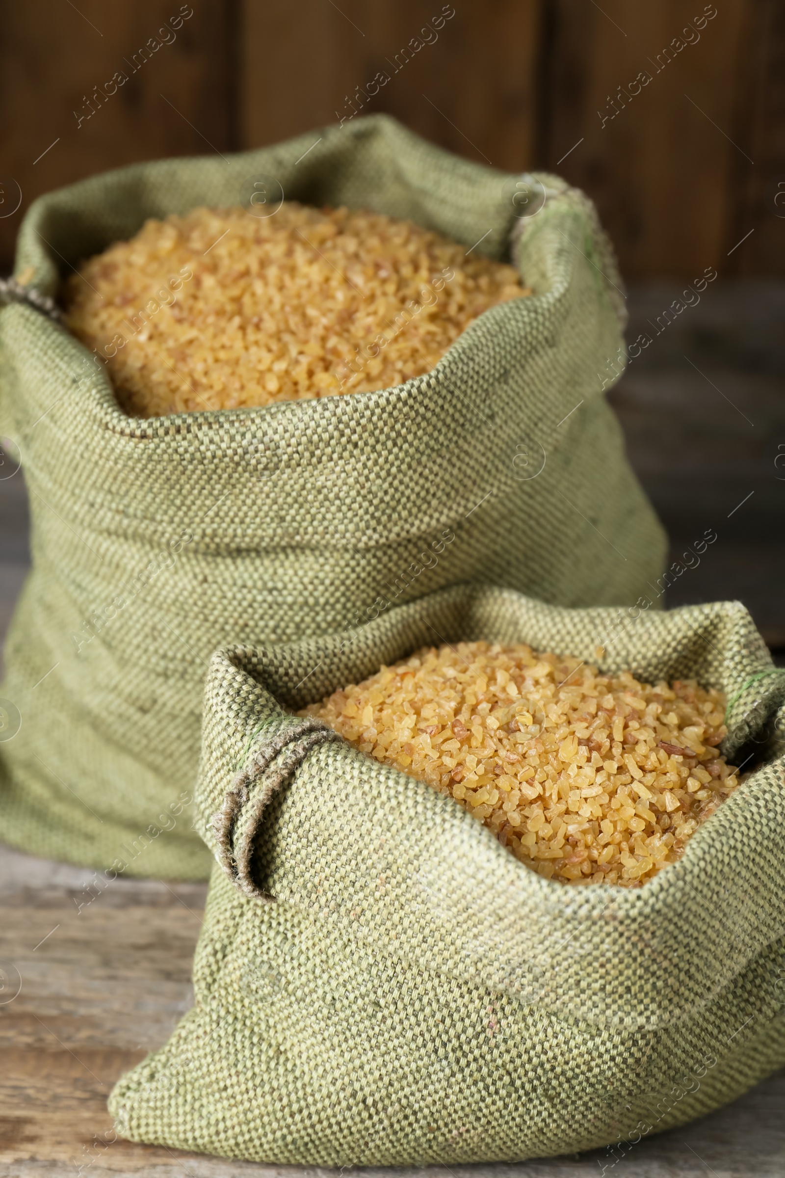 Photo of Burlap bags with uncooked bulgur on wooden table, closeup