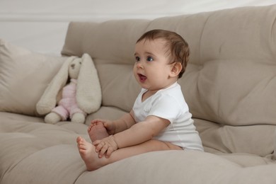 Photo of Cute little baby sitting on sofa at home