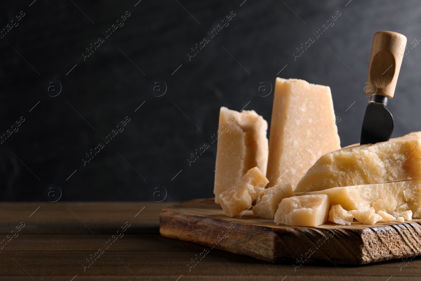 Photo of Pieces of delicious parmesan cheese with knife on wooden table. Space for text