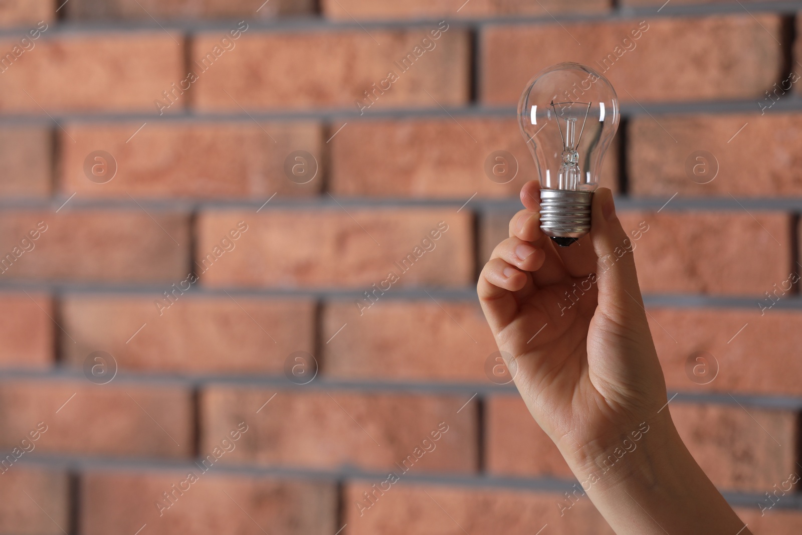 Photo of Woman holding light bulb near brick wall indoors, closeup. Space for text