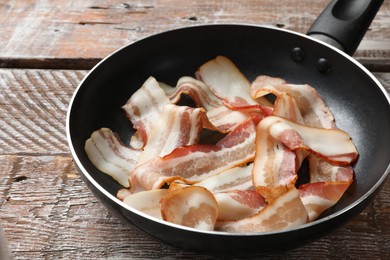 Delicious bacon slices in frying pan on wooden table, closeup