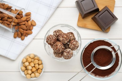 Tasty chocolate balls and ingredients on white wooden table, flat lay
