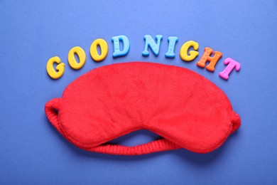 Photo of Soft sleep mask and words Good Night made of colorful letters on blue background, flat lay