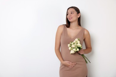 Beautiful pregnant woman in beige dress with bouquet of roses on white background, space for text