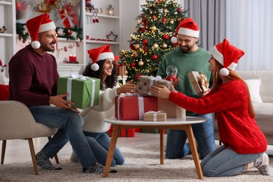 Photo of Christmas celebration. Happy friends in Santa hats exchanging gifts at home