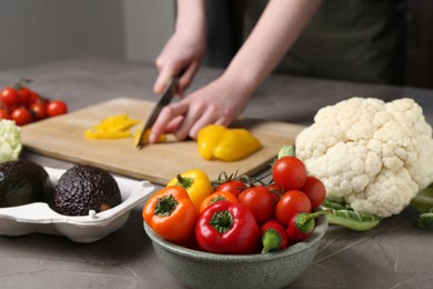 Photo of Healthy food. Woman cutting pepper at gray textured table, closeup