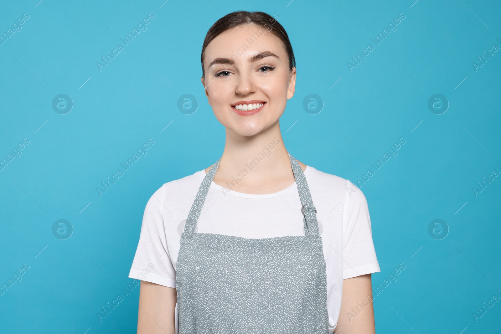 Photo of Beautiful young woman in clean apron with pattern on light blue background