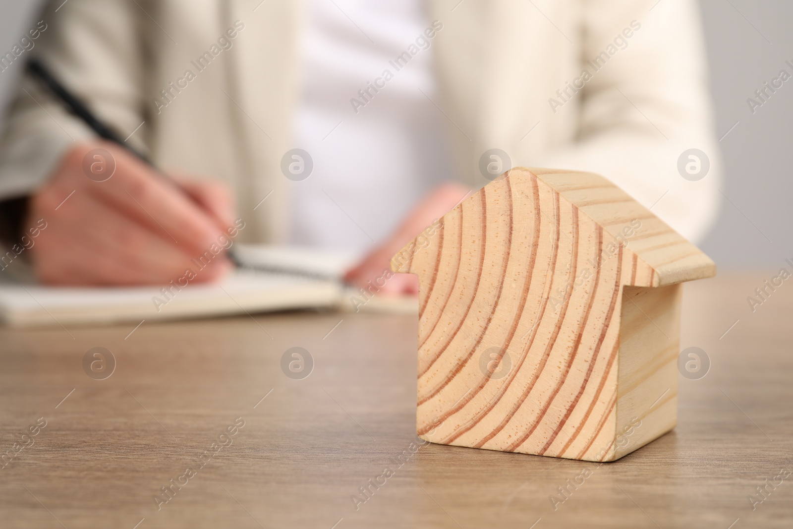 Photo of Mortgage concept. Woman writing at wooden table, focus on house model. Space for text