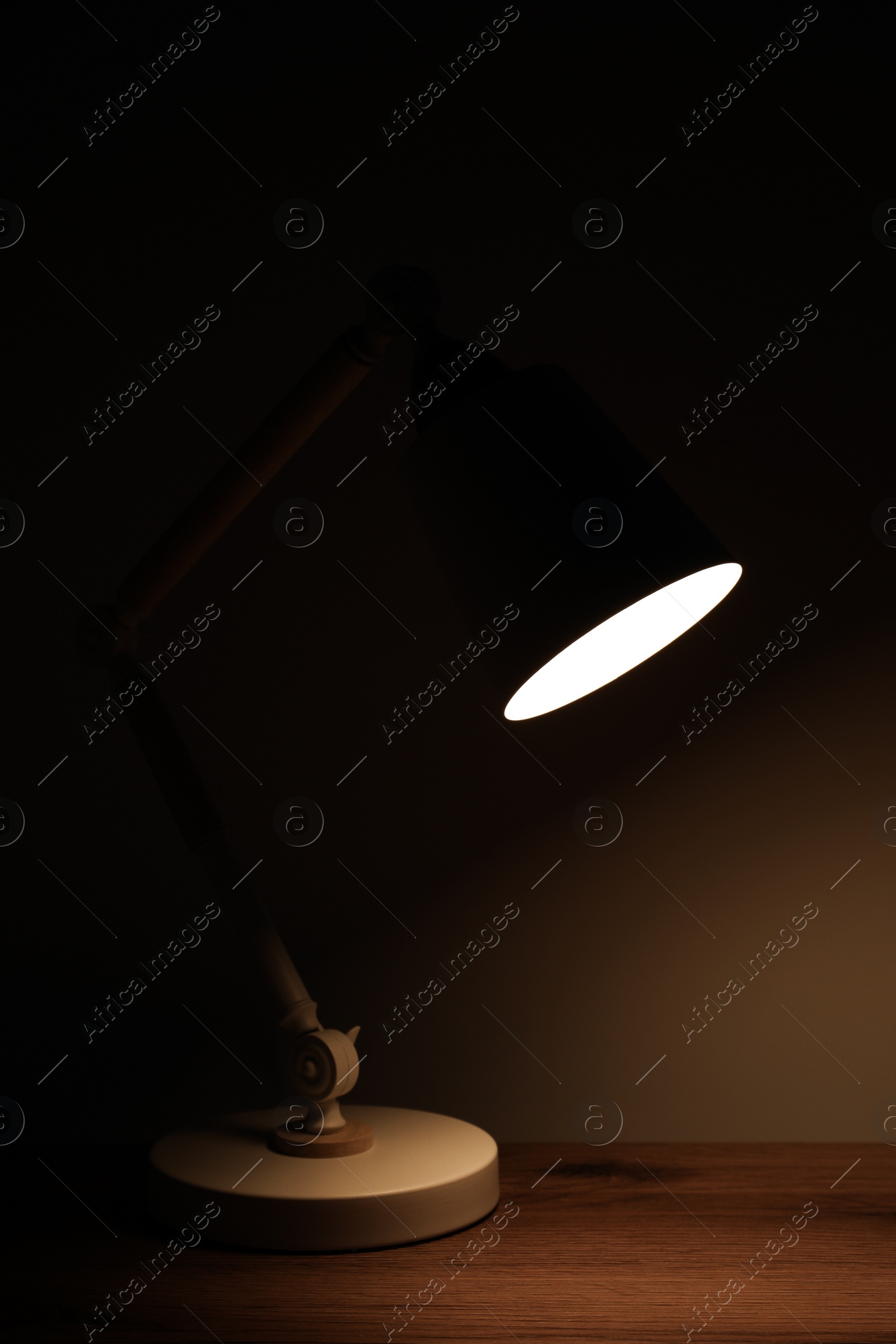 Photo of Stylish modern desk lamp on wooden table at night