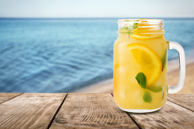 Image of Mason jar with lemonade on wooden table near sea, space for text