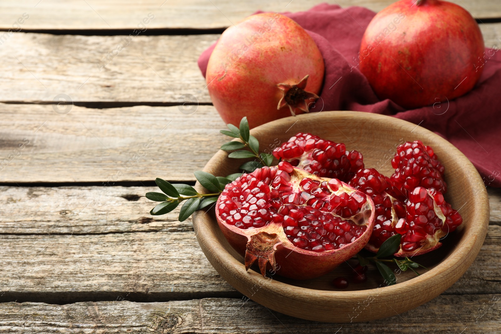 Photo of Fresh pomegranates and green leaves on wooden table, space for text