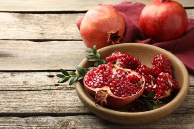 Photo of Fresh pomegranates and green leaves on wooden table, space for text