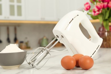 Photo of Modern mixer, eggs and bowl with flour on white marble table in kitchen