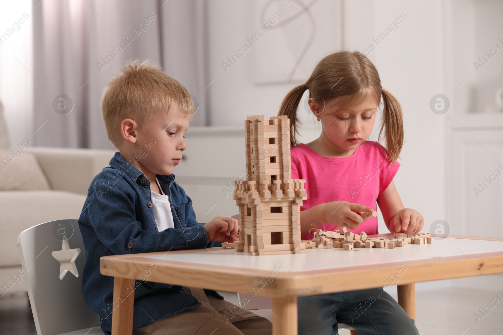 Photo of Little girl and boy playing with wooden tower at table indoors. Children's toy
