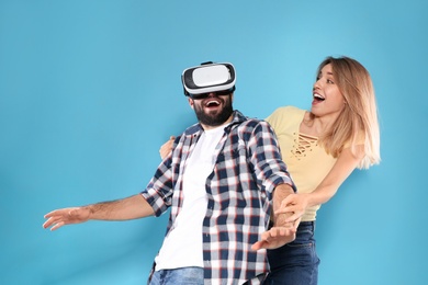 Young man playing video games with VR headset and emotional woman on color background