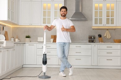 Photo of Happy man with steam mop showing thumbs-up in kitchen at home