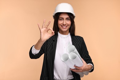 Architect in hard hat with drafts showing ok gesture on beige background