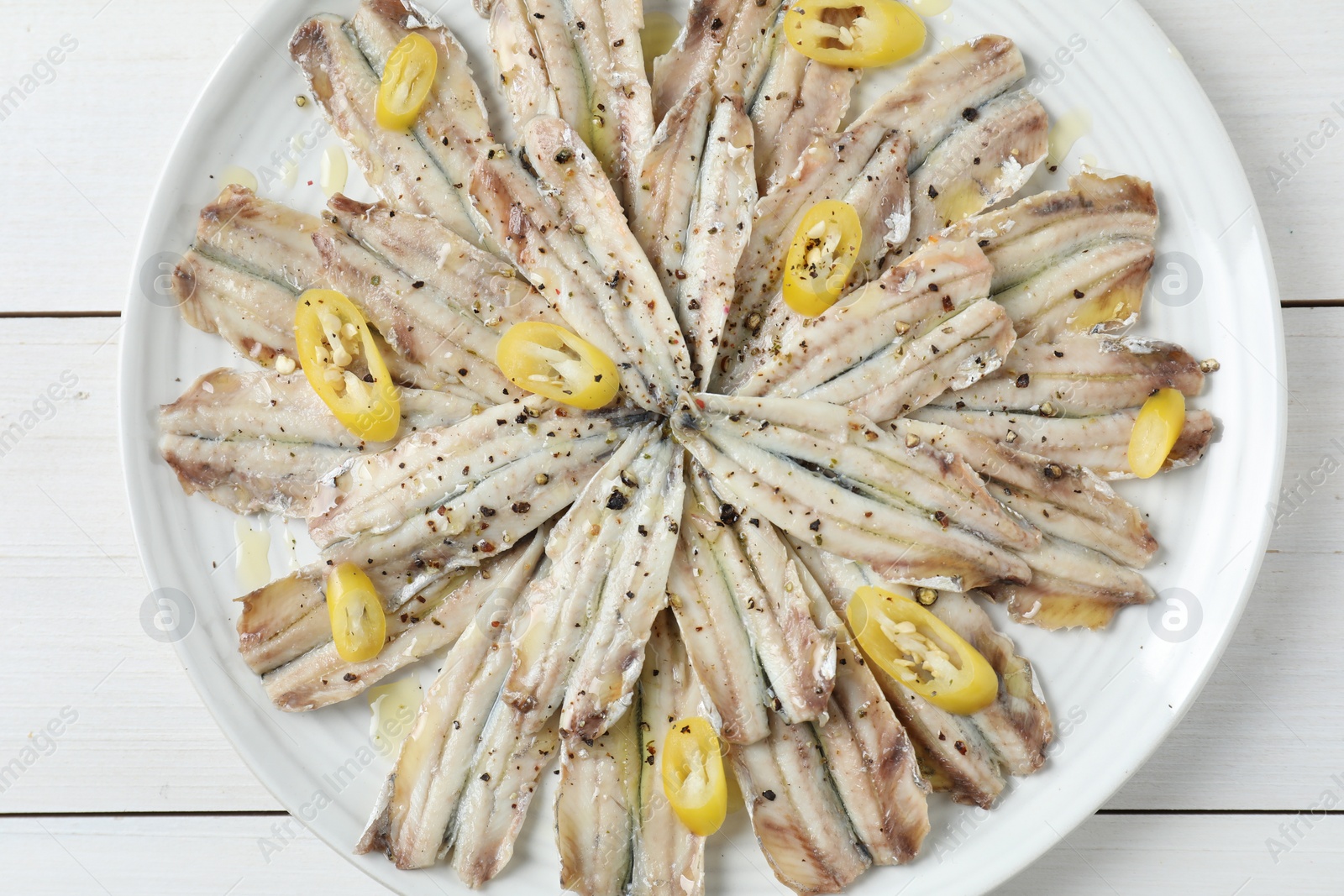 Photo of Tasty pickled anchovies with spices on white wooden table, top view