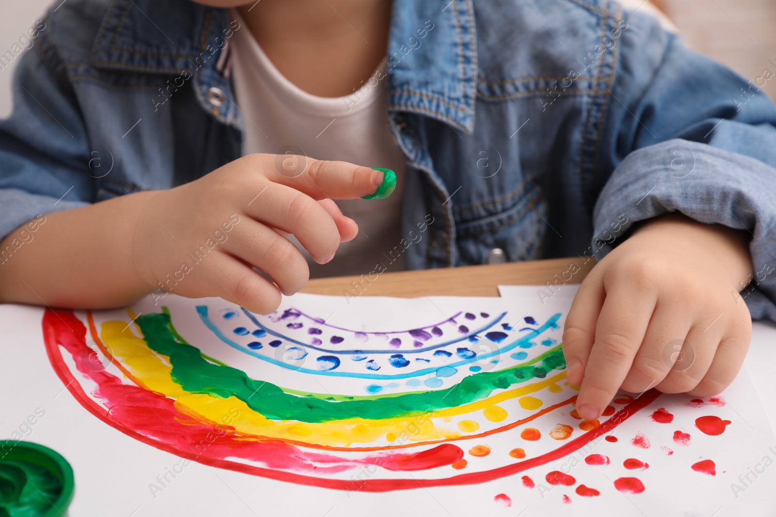 Photo of Little child painting with finger at wooden table indoors, closeup