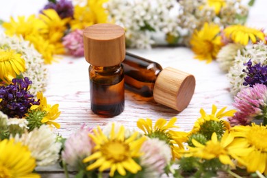 Photo of Bottles of essential oils surrounded by beautiful flowers on white wooden table, closeup