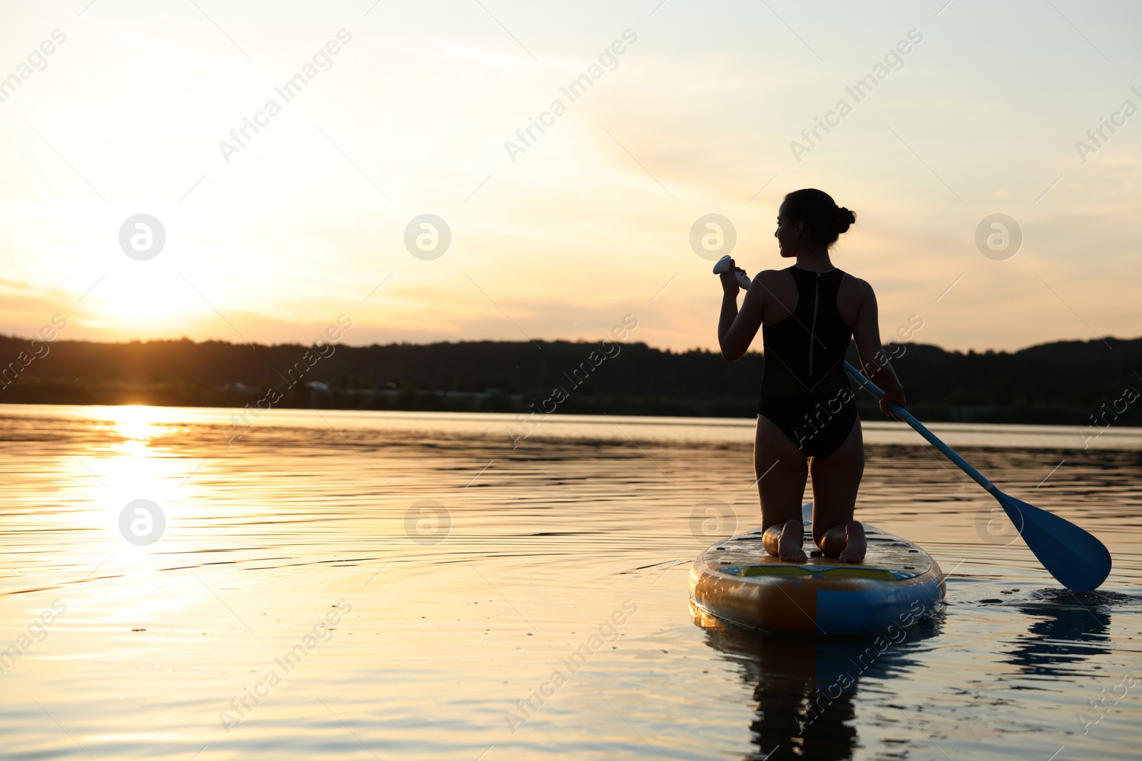 Photo of Woman paddle boarding on SUP board in river at sunset, back view