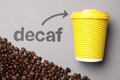 Coffee beans, word Decaf and arrow pointing at takeaway paper cup on light grey background, flat lay