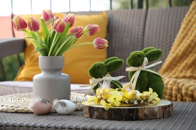 Terrace with Easter decorations. Bouquet of tulips in vase, bunny figures, decorative nest and eggs on table outdoors