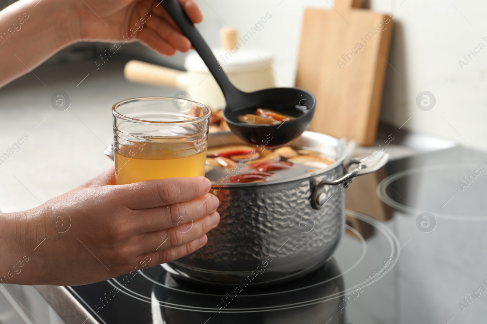 Photo of Woman pouring compot into glass near stove, closeup