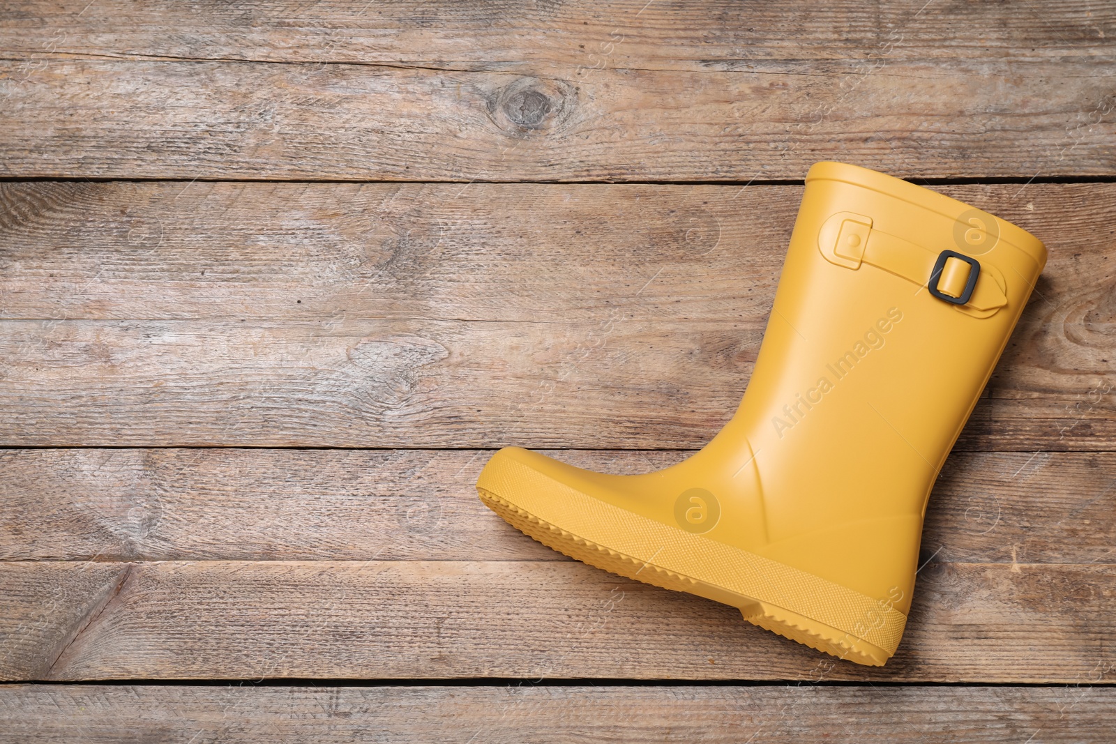 Photo of Yellow rubber boot on wooden background, top view. Space for text