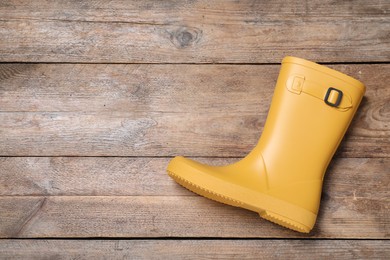 Photo of Yellow rubber boot on wooden background, top view. Space for text
