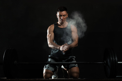 Photo of Strong man applying magnesium powder on hands before training with barbell in gym