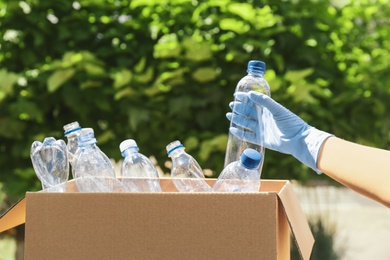 Photo of Woman putting used plastic bottle into cardboard box outdoors, closeup. Recycle concept