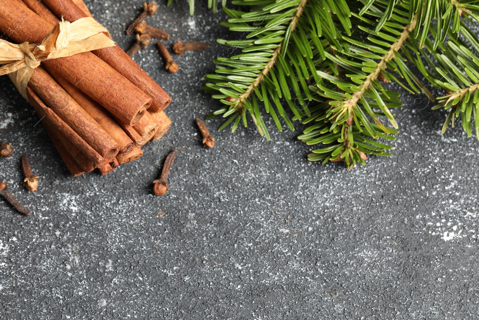 Photo of Different spices. Aromatic cinnamon sticks, clove seeds and fir branches on dark gray textured table, flat lay. Space for text